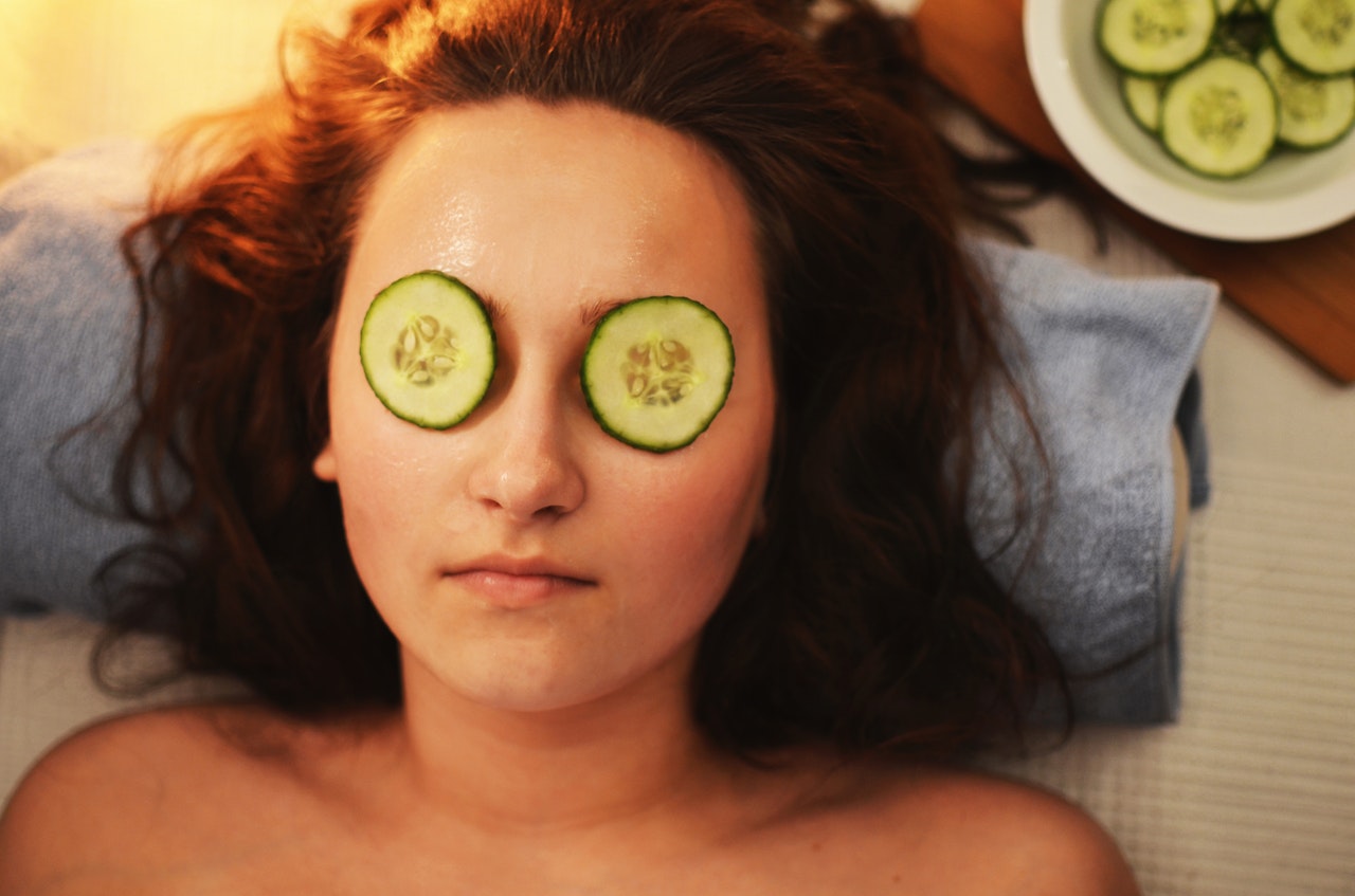a woman with slices of cucumber on her eyes